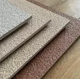 Textured carpet samples in beige and brown stacked on a wooden floor. They display a rough, detailed pattern, creating a cozy vibe.