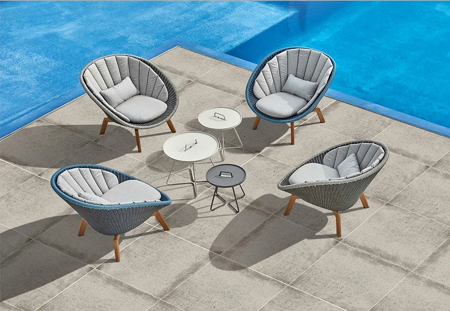 Four gray cushioned chairs and two round tables on a tiled patio by a blue pool, arranged in a circle under the bright sun.