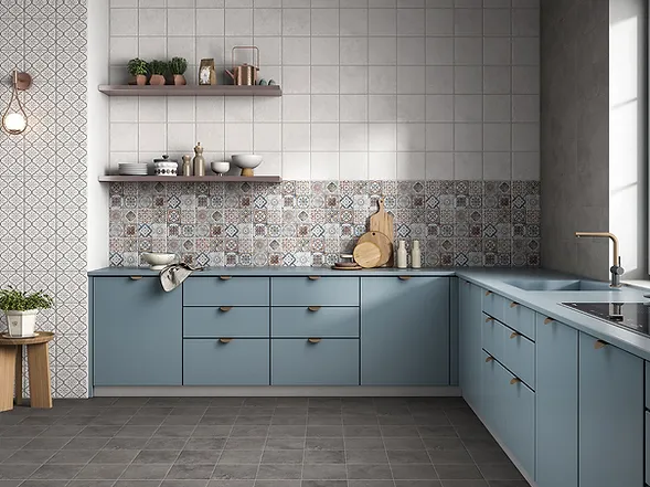 Modern kitchen with blue cabinets, patterned backsplash, grey floor, wooden cutting boards, and potted plants on shelves. Warm, cozy ambiance.