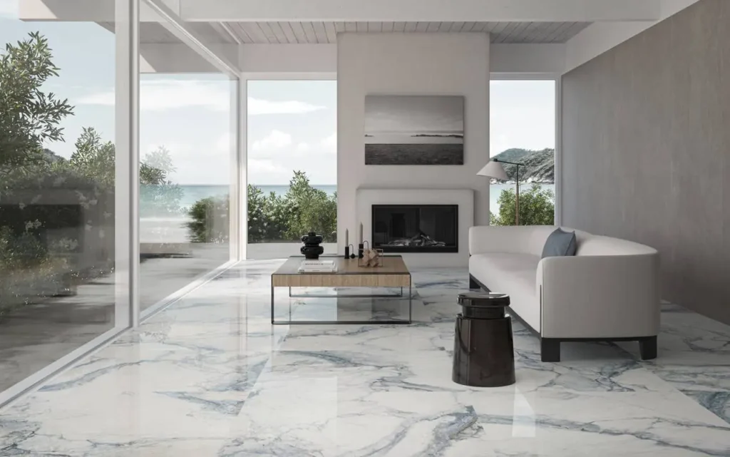 Modern living room with white sofa, marble floor, glass walls, and ocean view. Minimalist decor, black and white photo above fireplace.