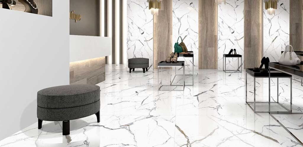 Interior showroom with white marble-look tile flooring, gray ottomans, and display tables.